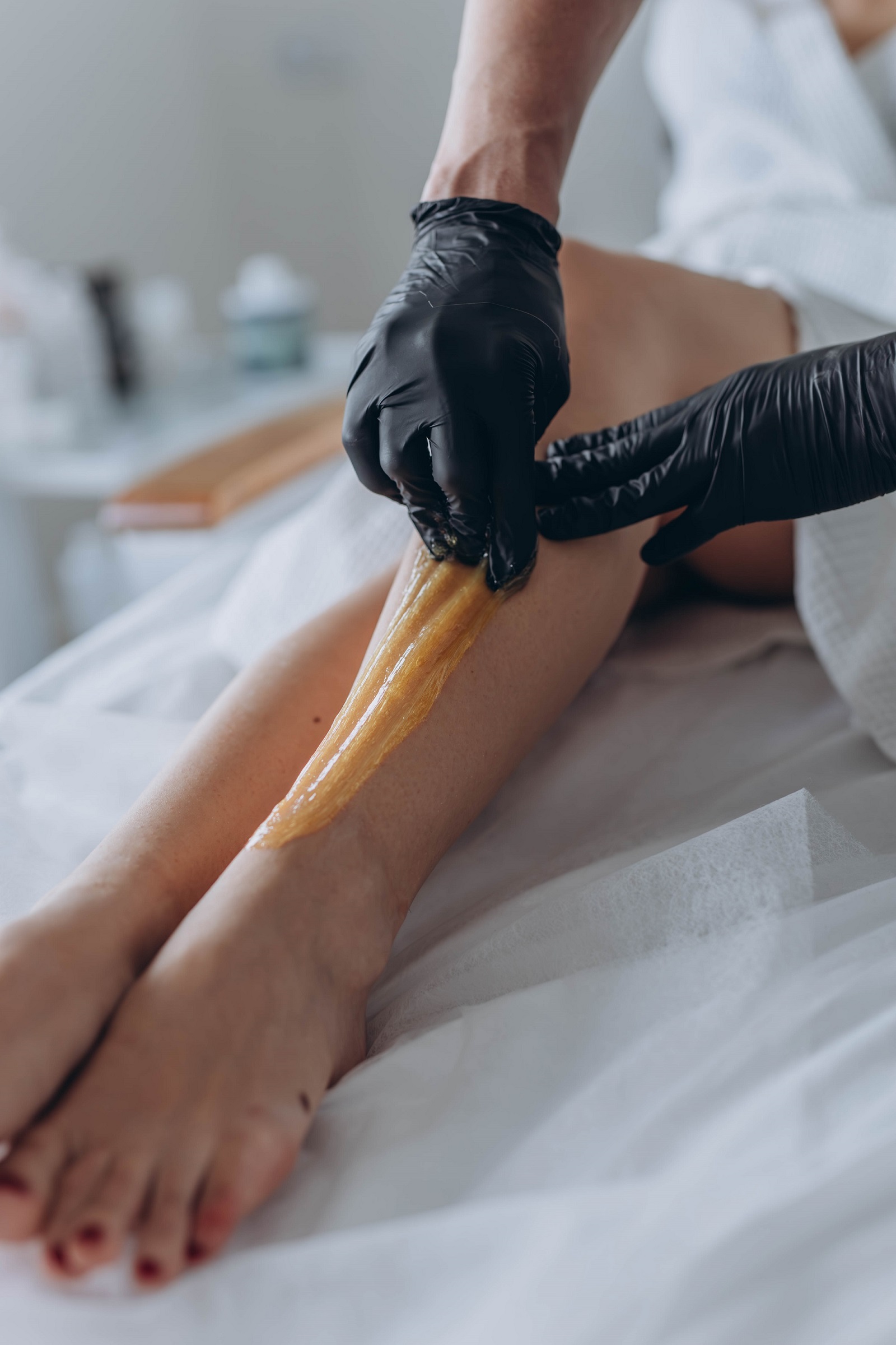 Beautician depilating young woman's legs with liquid sugar in spa center. High quality photo